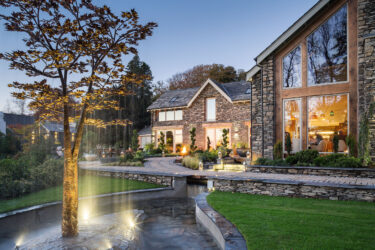 Exterior of Gilpin Spice at dusk, with warm light glowing through the restaurant windows and landscaped gardens surrounding the stone building.