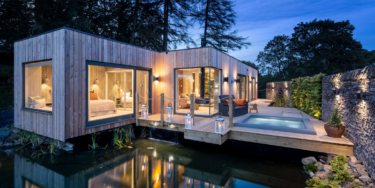 Gilpin Spa Suite exterior at dusk, with floor-to-ceiling windows, a private terrace and outdoor hot tub beside the water.