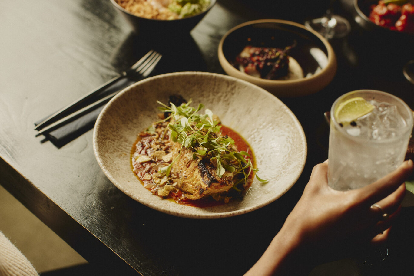 Gilpin Spice's tandoori hispi cabbage served in a rich spiced sauce, topped with fresh herbs and crispy garnish, alongside a lime cocktail
