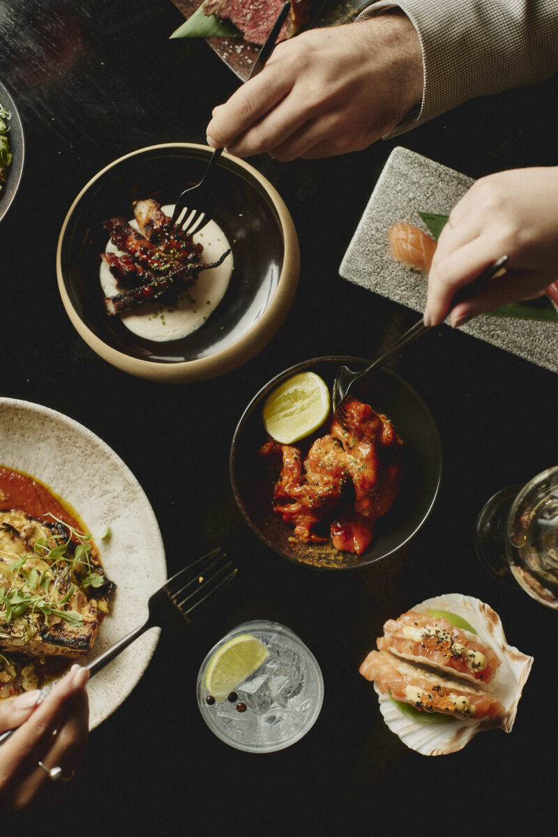 Diners sharing a selection of Gilpin Spice dishes, including spice fried chicken, sushi, grilled seafood and tacos.