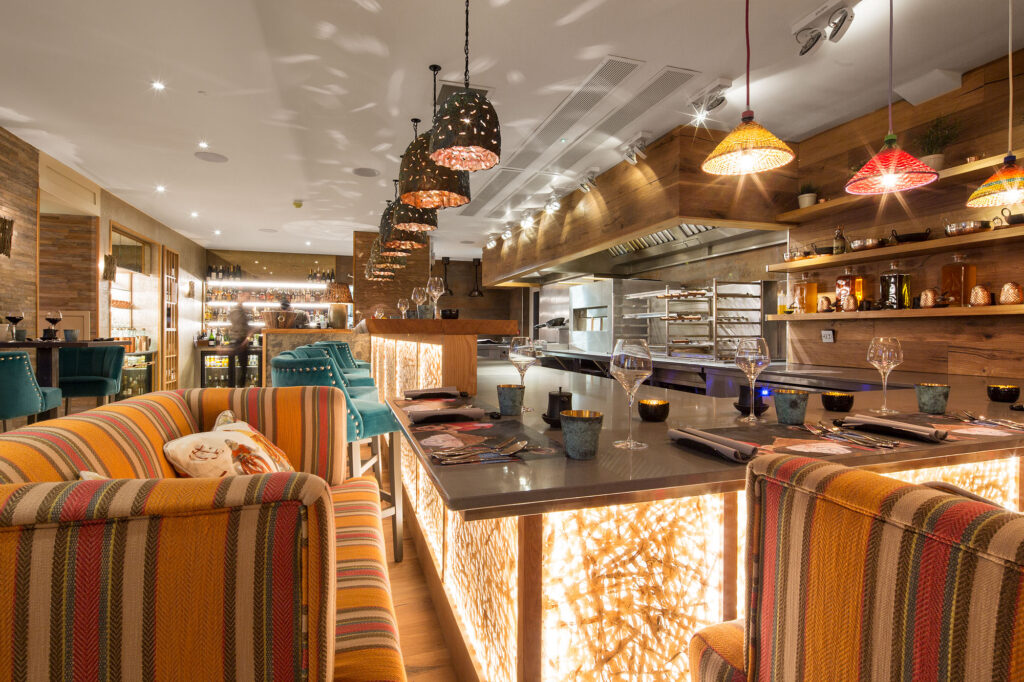 Gilpin Spice’s Malaysia Room, with colourful upholstered seating, laid dining tables, pendant lights and an open kitchen.