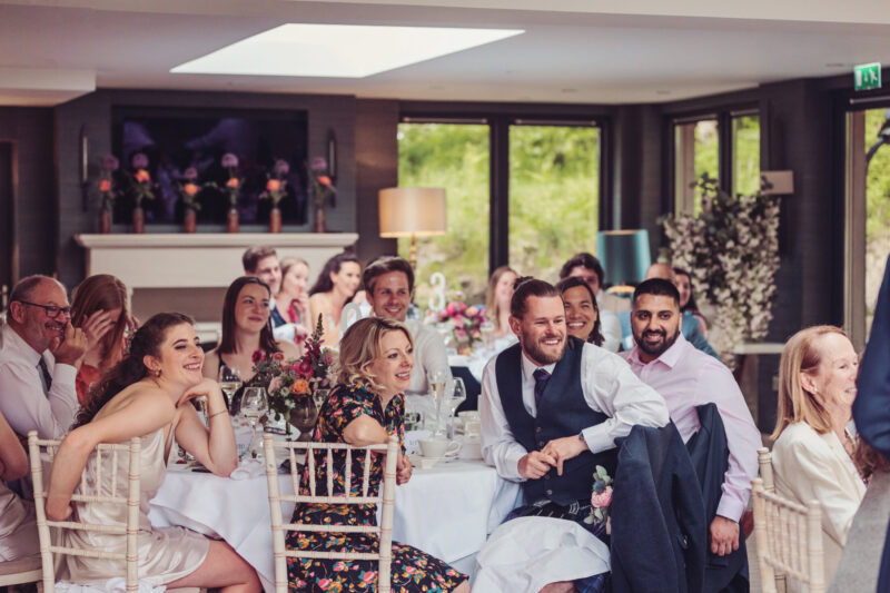 : Wedding guests laughing and celebrating around beautifully dressed tables during a lively wedding reception at Gilpin.