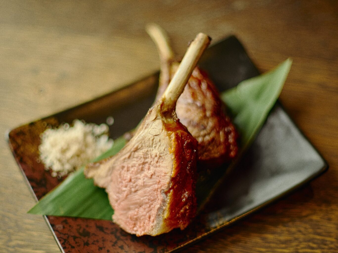 Gilpin Spice's lamb, sliced to reveal a pink centre, served on the bone with a crisp browned exterior on a ceramic plate.