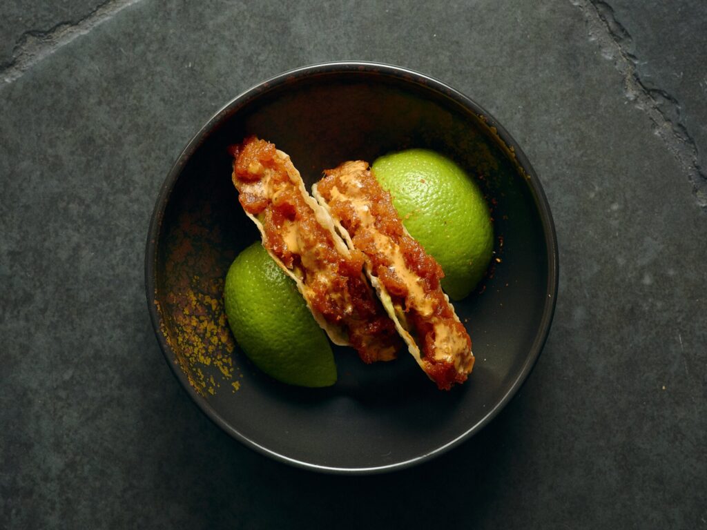 Gilpin Spice's sushi tacos filled with fresh fish and spicy sauce, served with lime wedges in a dark ceramic bowl