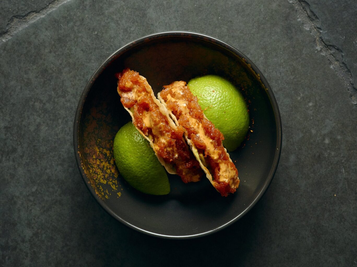 Gilpin Spice's sushi tacos filled with fresh fish and spicy sauce, served with lime wedges in a dark ceramic bowl
