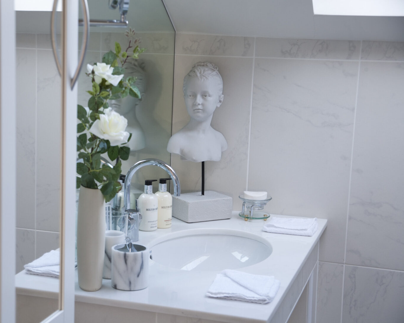 Maud Room bathroom at Gilpin Lake House with a white vanity, fresh flowers, luxury toiletries and decorative details.