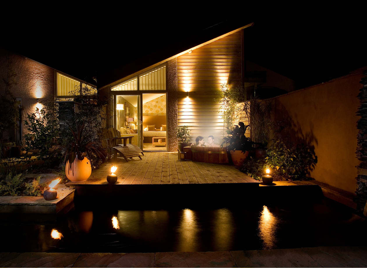 Gilpin Garden Suite exterior at night, with warm interior lighting, a private terrace and illuminated garden beside the water.
