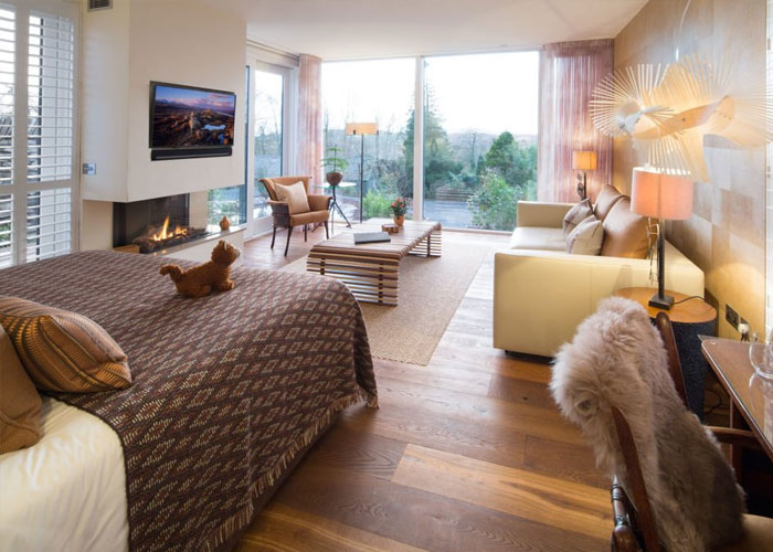 Interior of a Gilpin Spa Lodge with a spacious bedroom, lounge area and floor-to-ceiling windows overlooking the gardens.