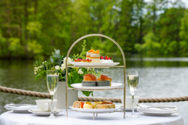 Afternoon tea with sandwiches, scones and colourful cakes served with glasses of Champagne beside the lake at Gilpin Lake House