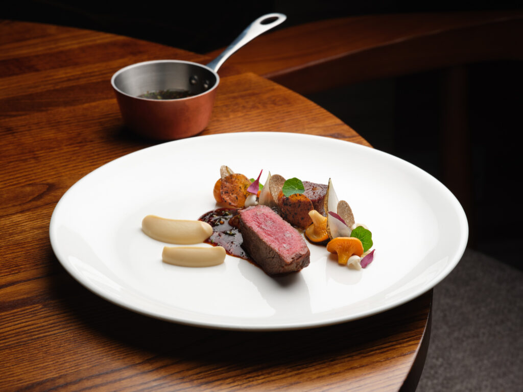 SOURCE at Gilpin Hotel's beef, served pink with mushrooms, roasted vegetables, purée and a rich sauce on a white plate.