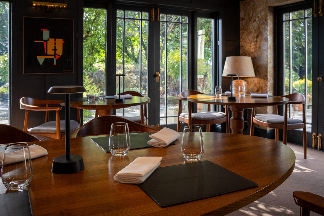 SOURCE dining room at Gilpin Hotel in summer, with tables set beside large windows overlooking the green gardens.