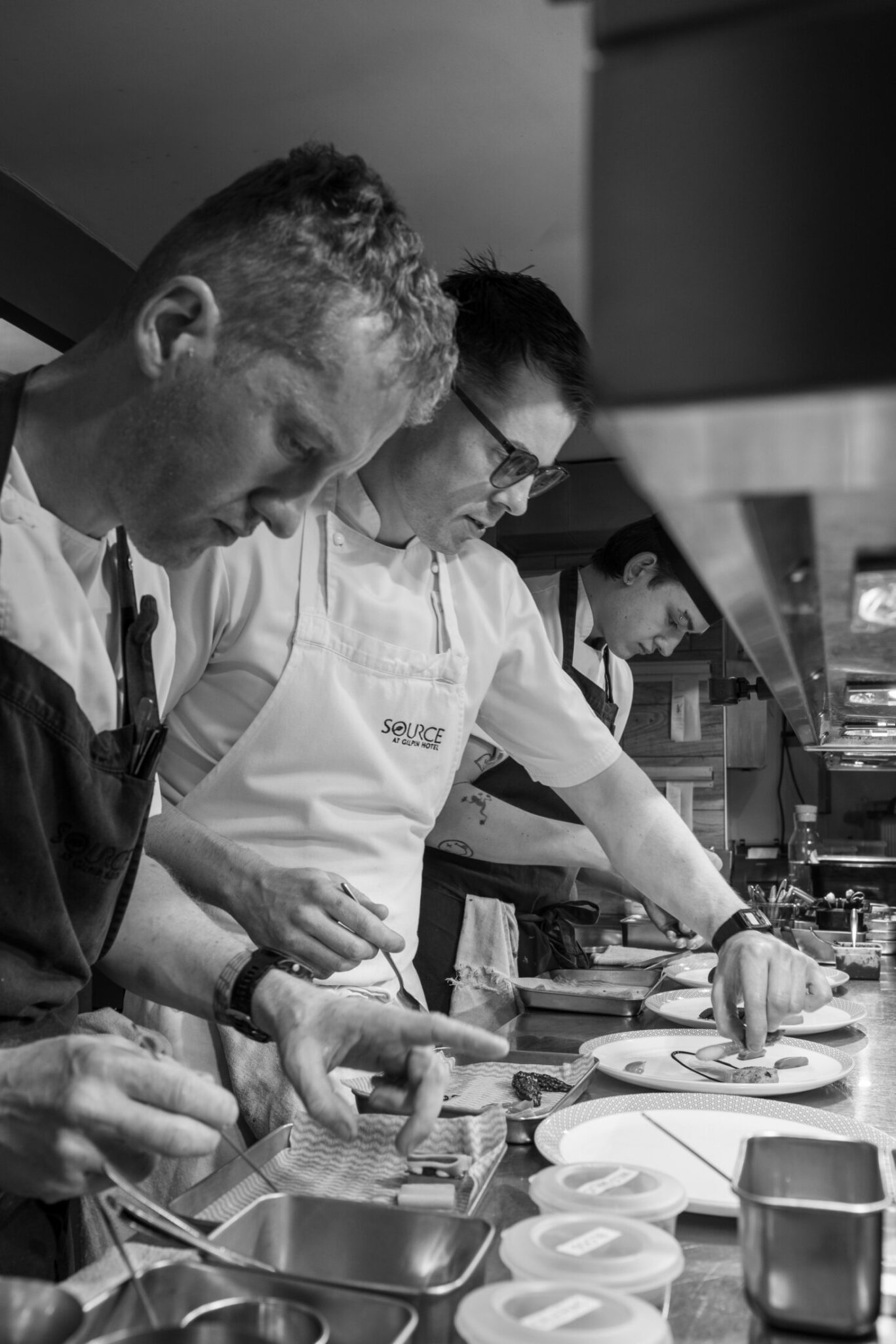 SOURCE chefs carefully plating dishes together in the restaurant kitchen at Gilpin Hotel.
