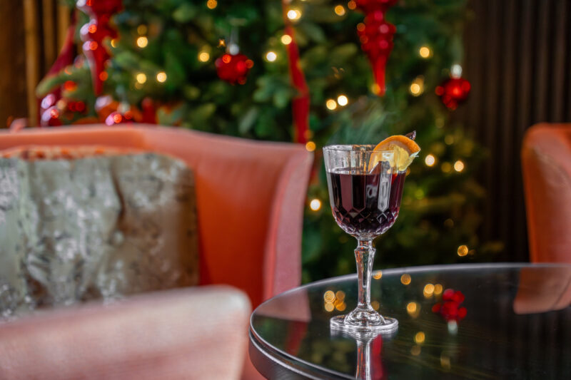 Glass of mulled wine with orange garnish on a table beside a decorated Christmas tree at Gilpin Hotel