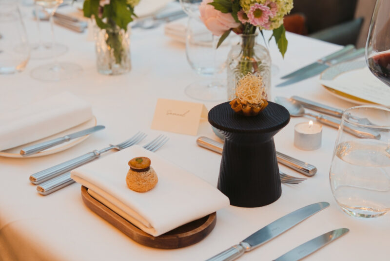 Fine dining table setting at SOURCE, with an elegant canapé presentation, fresh flowers and neatly arranged glassware and cutlery.