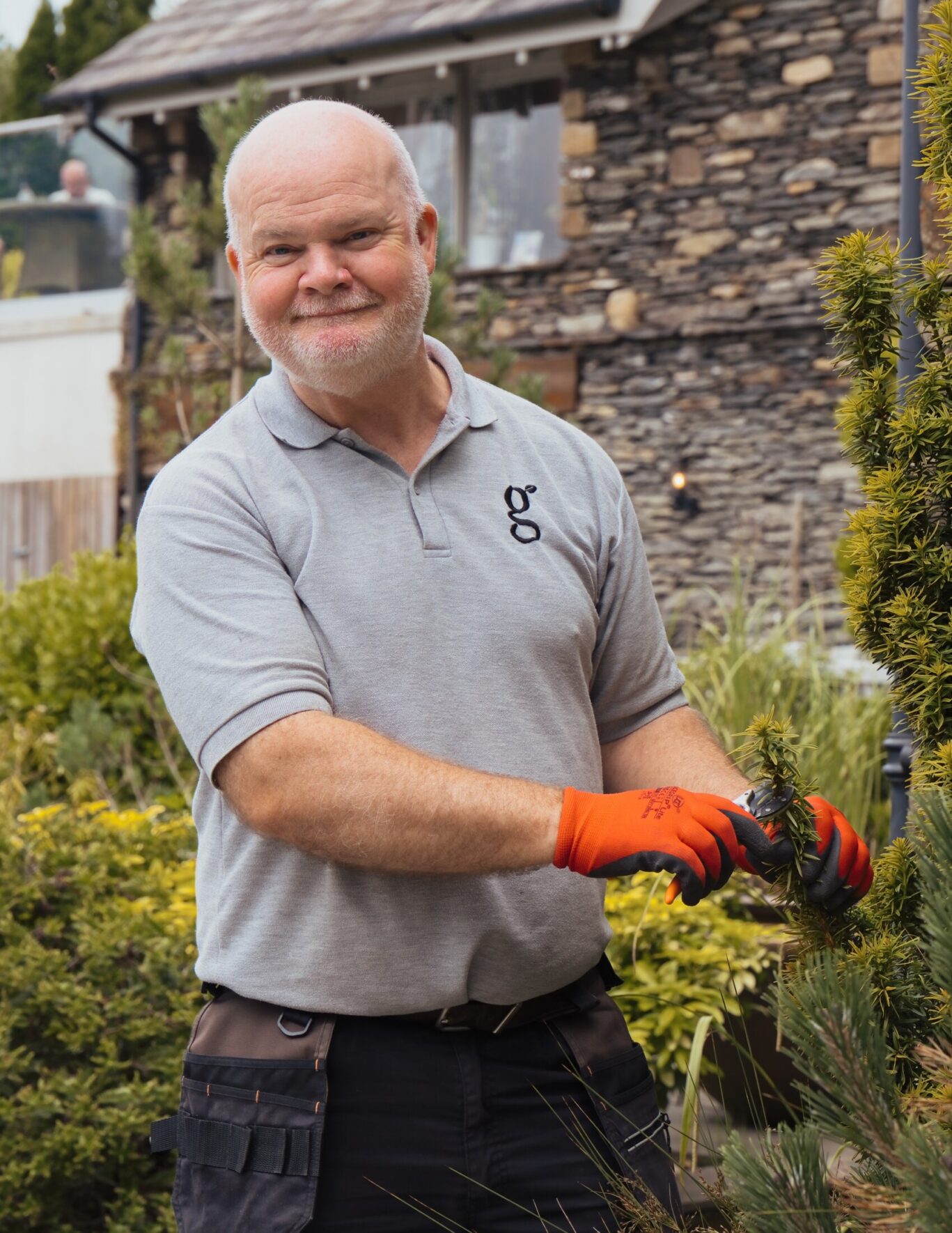 Gilpin Hotel gardener smiling while pruning a shrub with secateurs in the hotel gardens.