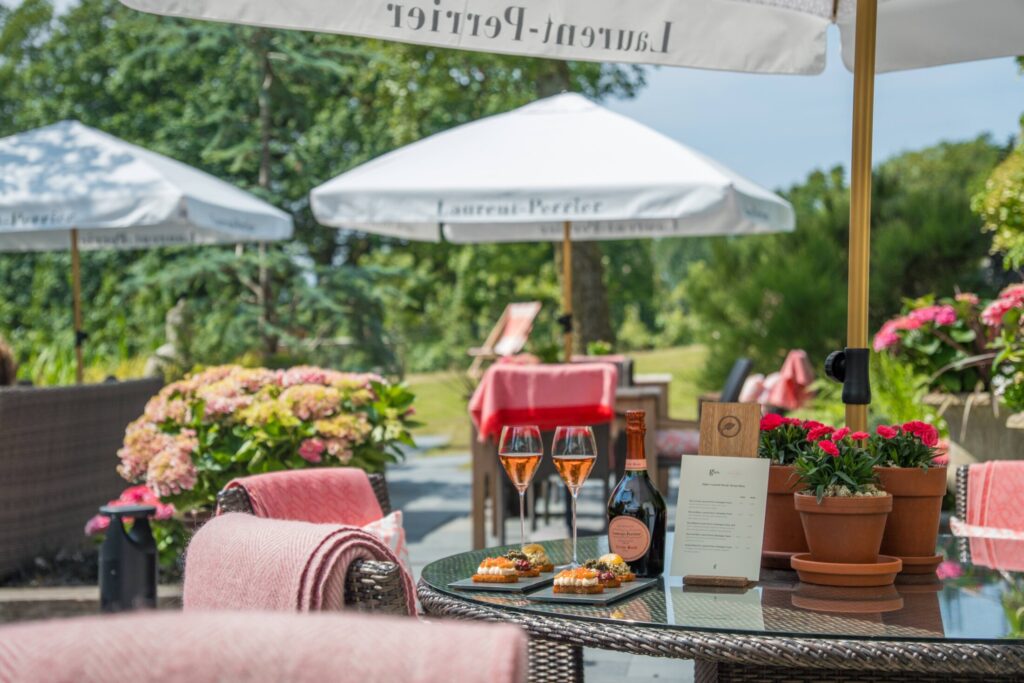 Sunny garden terrace at Gilpin Hotel with outdoor seating, colourful flowers and drinks served beneath parasols.