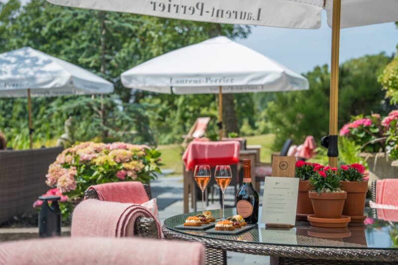 Sunny garden terrace at Gilpin Hotel with outdoor seating, colourful flowers and drinks served beneath parasols.