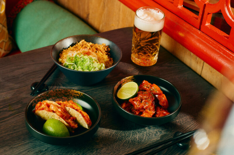 Gilpin Spice dishes including sushi tacos, spice fried chicken and a rice bowl, served with lime and a glass of beer.