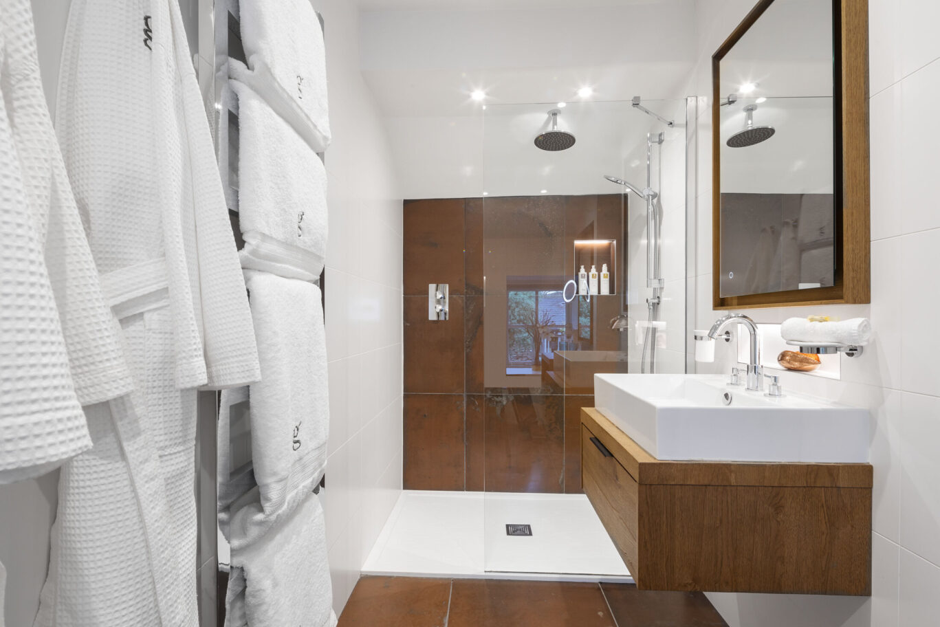 Rydal Classic Room bathroom at Gilpin Hotel with a walk-in rainfall shower, vanity and contemporary wood finishes.