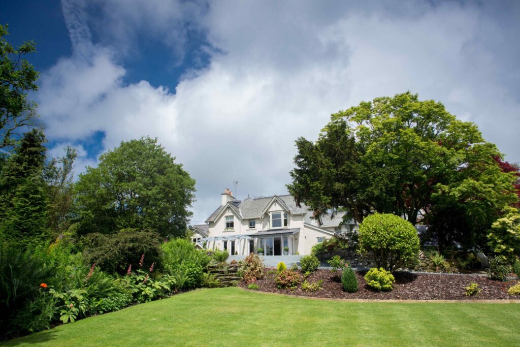 Exterior of Gilpin Hotel surrounded by landscaped gardens, mature trees and a sweeping green lawn.