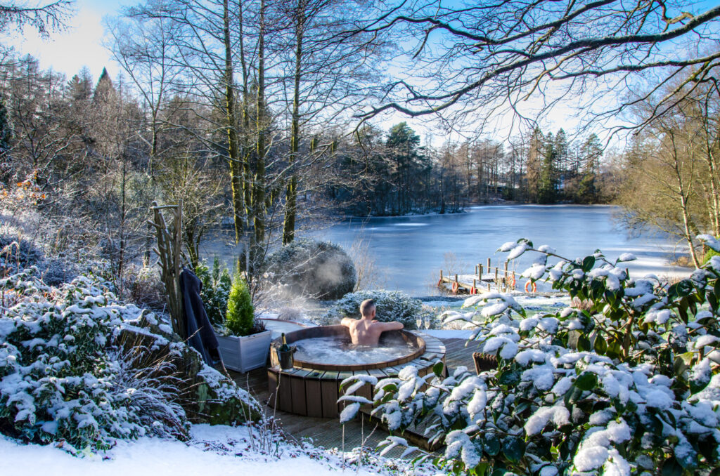 Guest relaxing in a steaming hot tub overlooking frozen Knipe Tarn and snowy woodland at Gilpin Lake House.