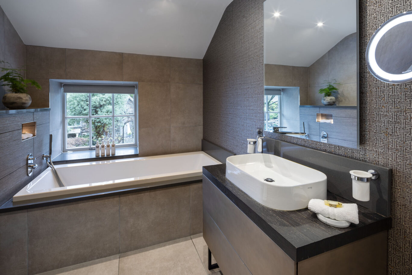 Cleabarrow Master Room bathroom at Gilpin Hotel with a large bath, modern vanity, illuminated mirror and contemporary tiled finishes.