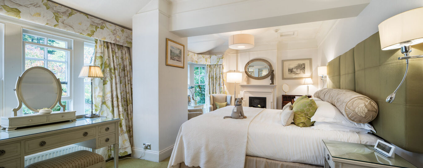 Crosthwaite Master Room at Gilpin Hotel with a king-size bed, soft green furnishings and dressing table beside the window.