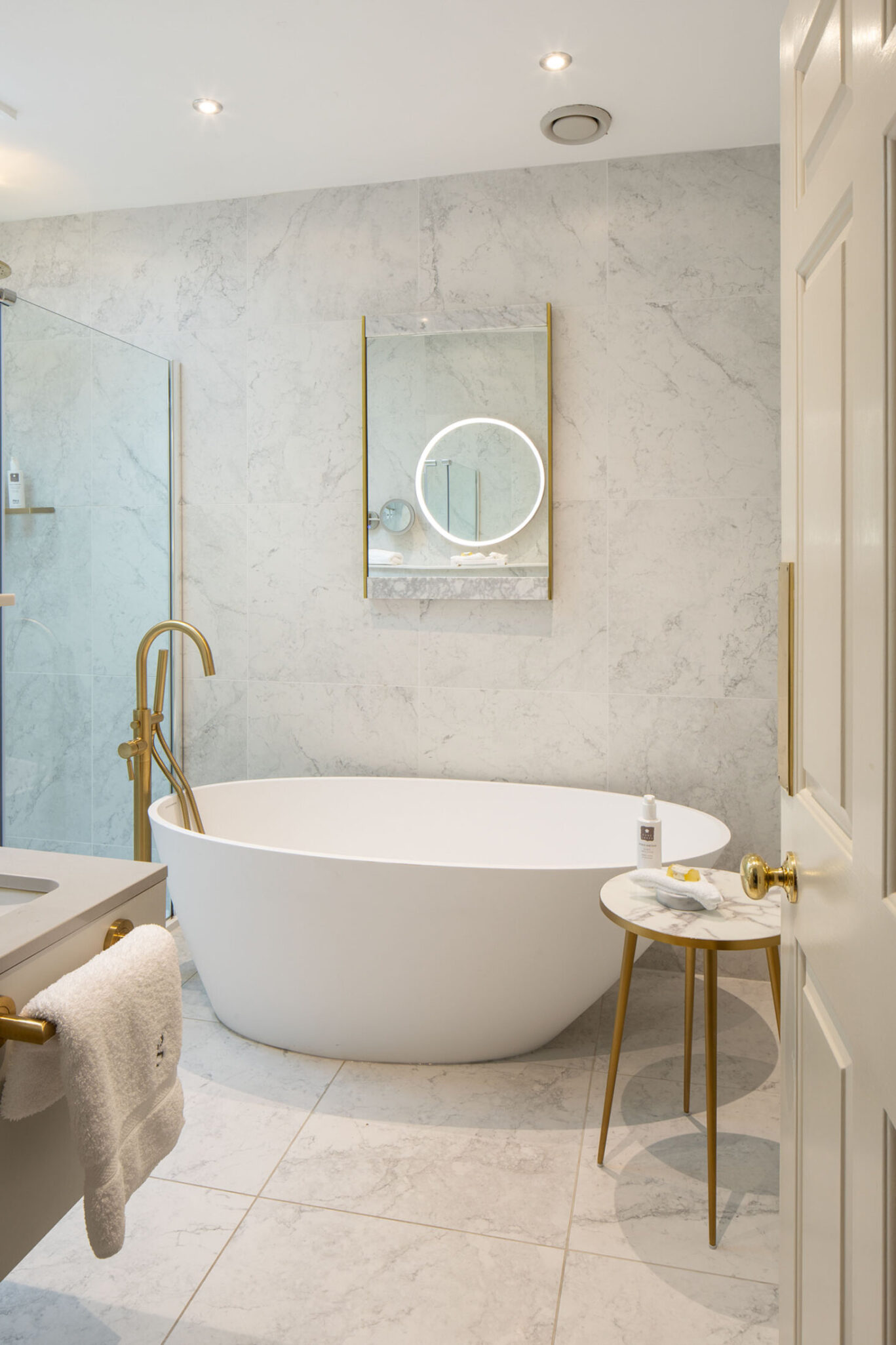 Grasmere Junior Suite bathroom at Gilpin Hotel with a freestanding bath, walk-in shower, marble-effect tiles and gold fittings.