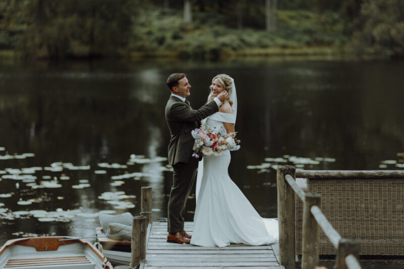 Bride and groom standing together on a lakeside jetty at Gilpin Lake House on their wedding day.