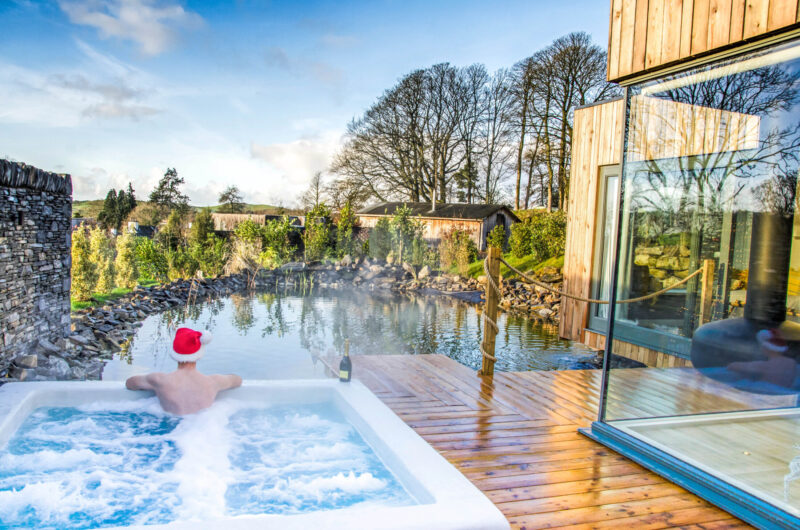 Man wearing a Santa hat relaxing in a private Spa Lodge hot tub overlooking a natural pond and woodland at Gilpin Hotel
