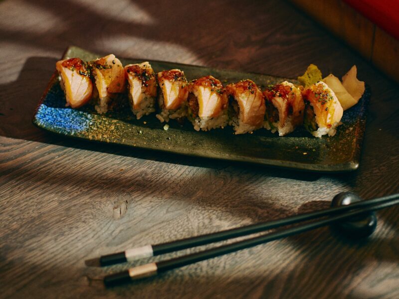 Eight pieces of sushi topped with seared salmon and seasoning on a rectangular ceramic plate, with ginger and wasabi at the side.
