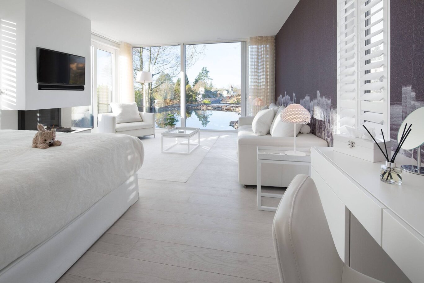 Bright Spa Lodge bedroom and lounge with contemporary white interiors, fireplace and floor-to-ceiling windows overlooking the gardens