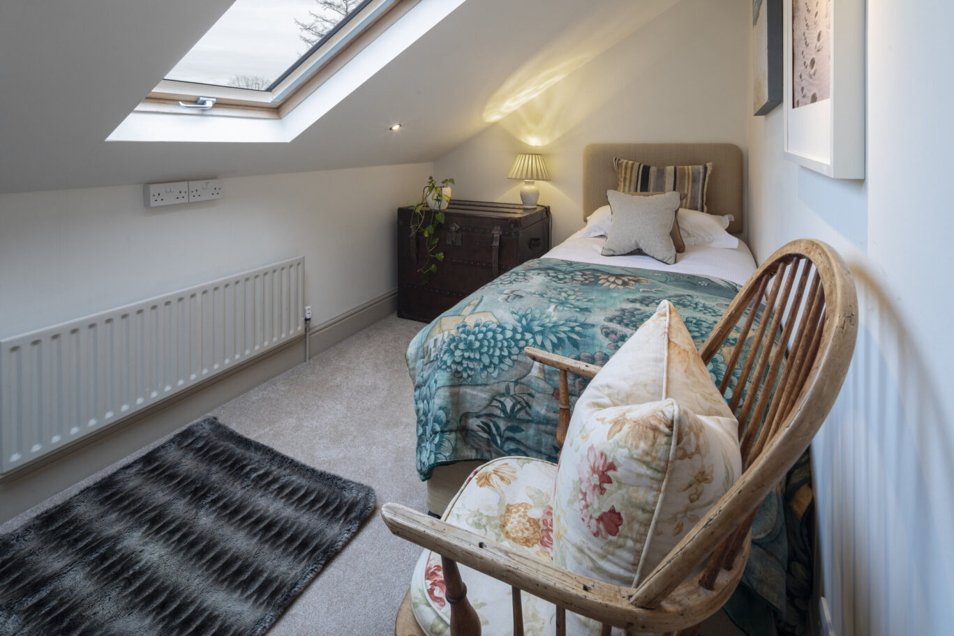 Cosy single bedroom at Gilpin Lake House with a floral bedspread, skylight and comfortable wooden armchair.