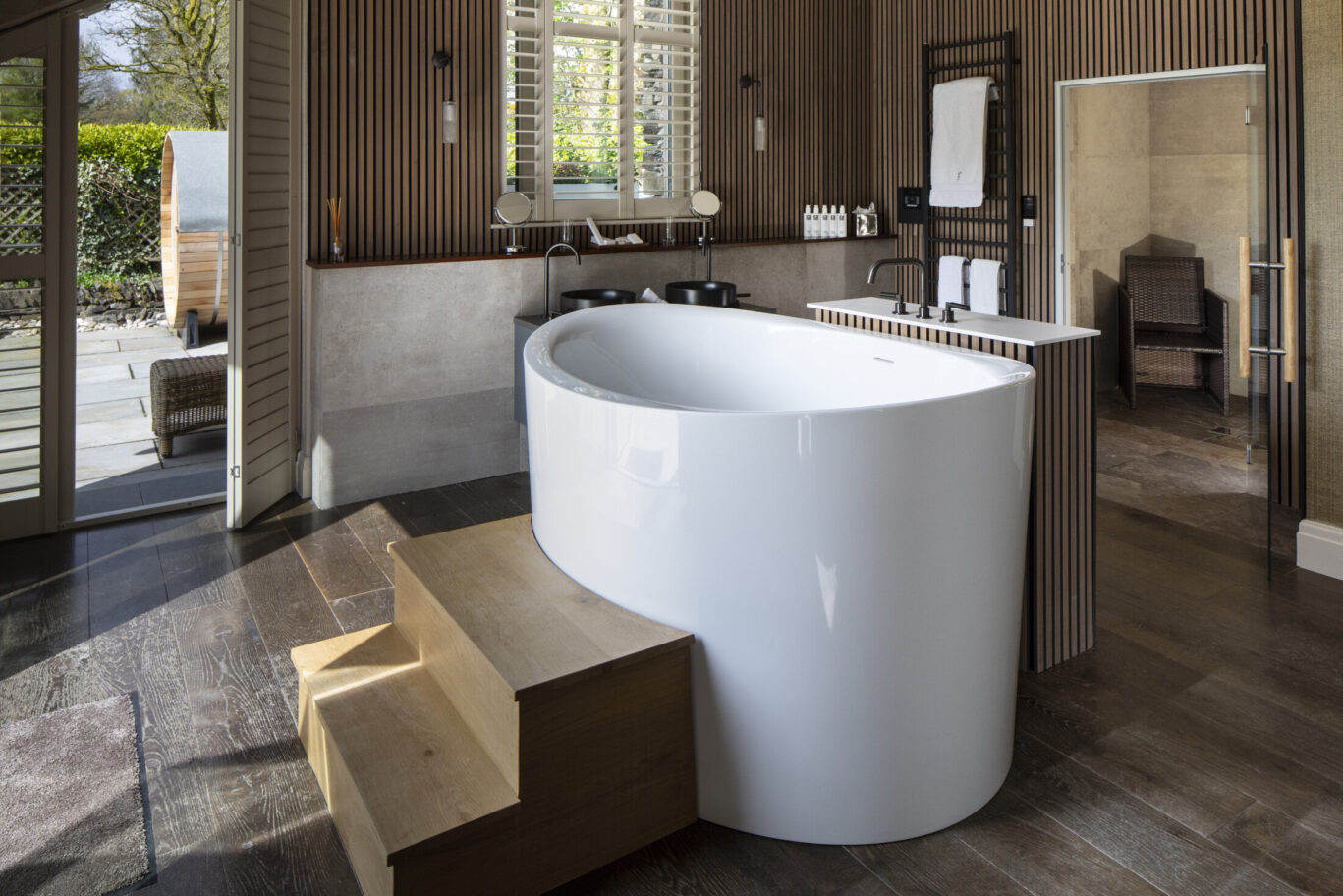 Luxury bathroom at Gilpin Lake House with a freestanding bath, warm wood finishes and doors opening onto a private terrace.