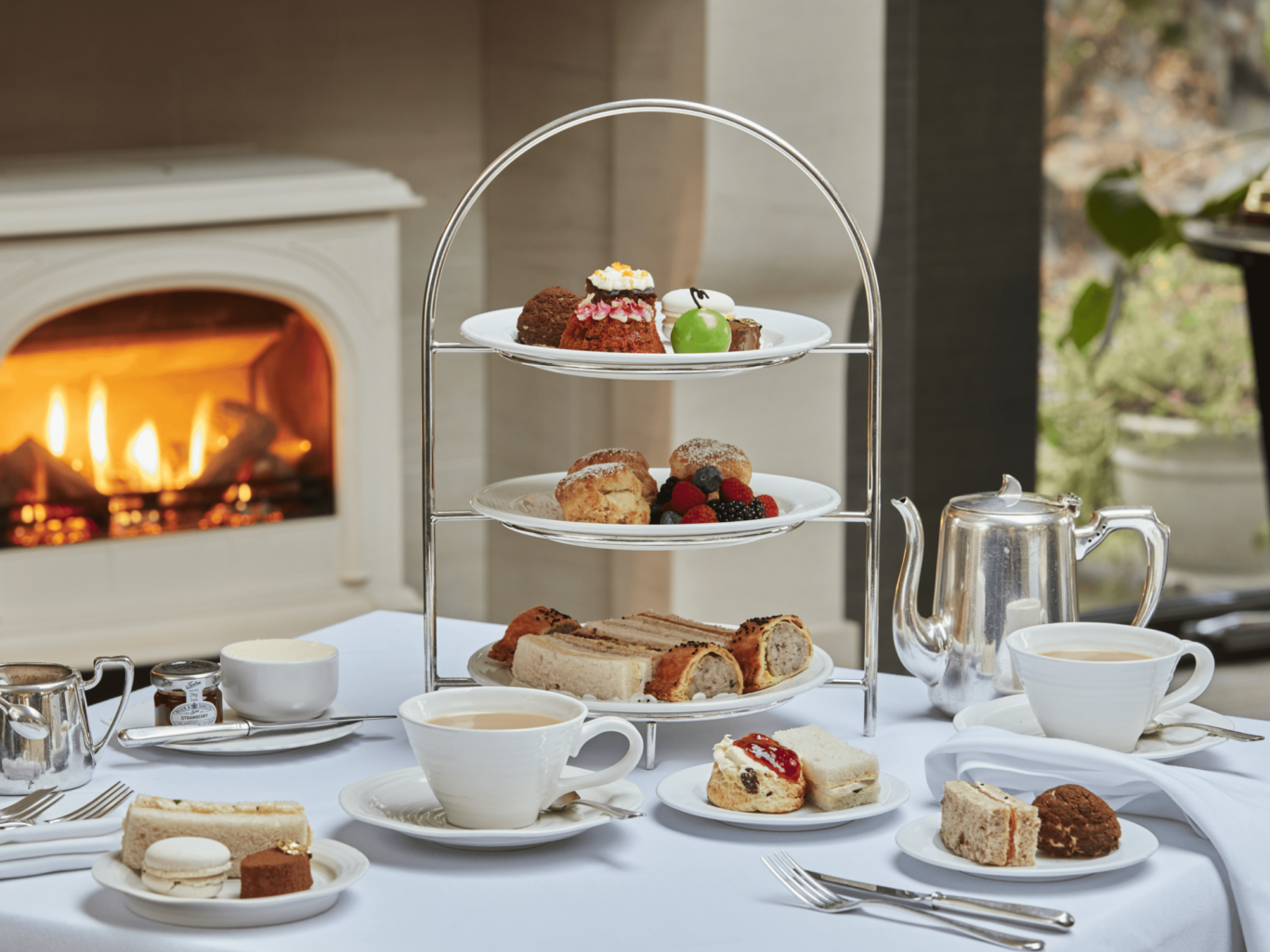 Gilpin Hotel afternoon tea with finger sandwiches, scones, cakes and tea served on a tiered stand beside a glowing fireplace