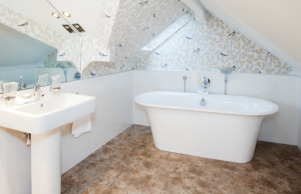 Wetherlam Master Room bathroom at Gilpin Hotel with a freestanding bath, large mirror and bird-patterned wallpaper.