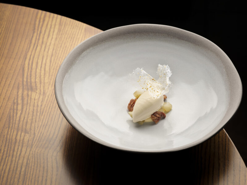 SOURCE at Gilpin Hotel's fennel mousse served with pecans, pieces of fruit and a delicate crisp garnish in a wide ceramic bowl.